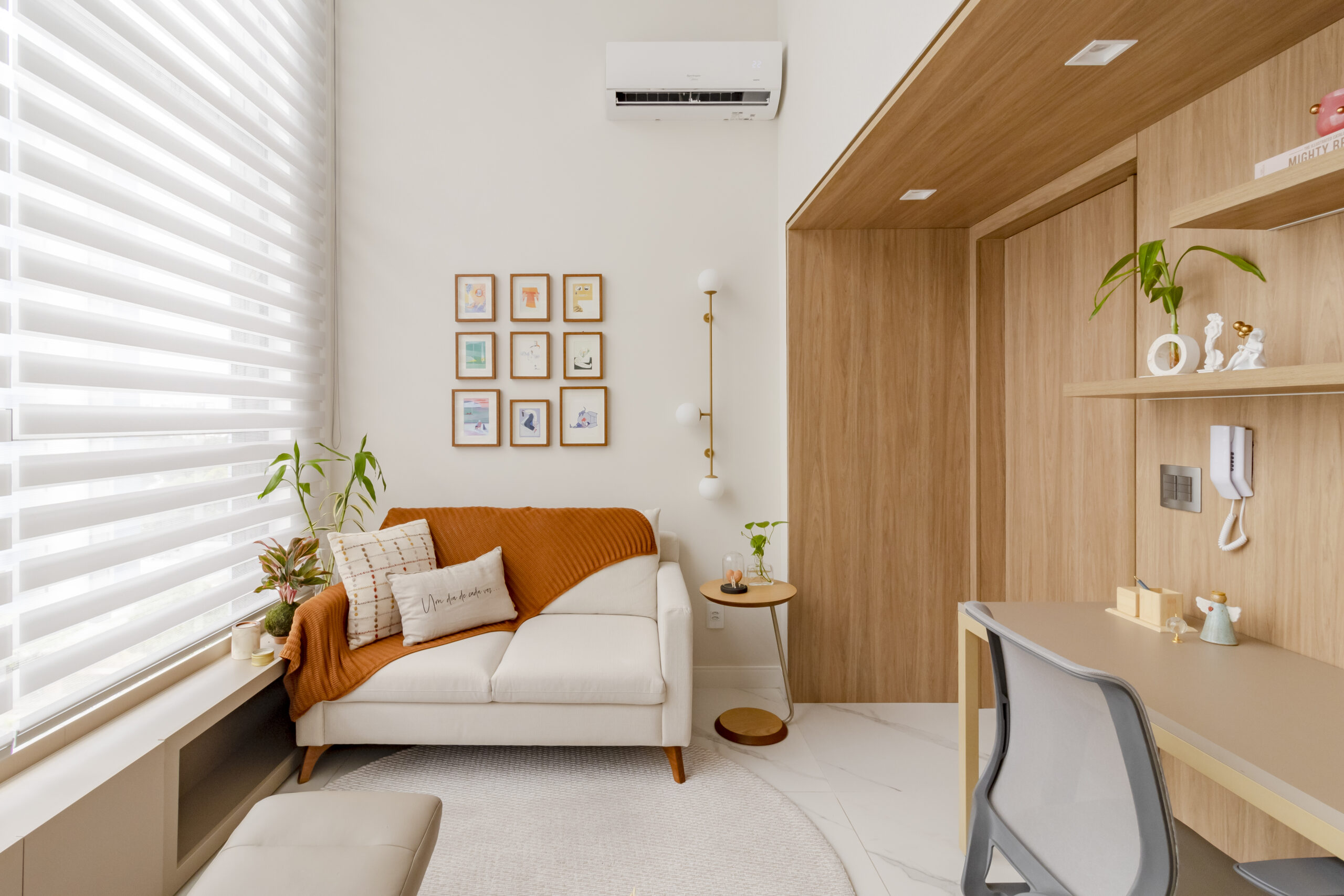 Ambiente aconchegante e moderno com cortina Mystique da Uniflex, projetado pela arquiteta Elisa Coelho. O espaço integra home office e área de descanso, com tons neutros, detalhes em madeira e iluminação natural suave filtrada pela cortina.