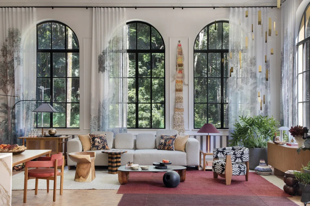 Ambiente PN+ Paula Neder – Carmim na CASACOR São Paulo 2026, com cortinas estampadas translúcidas, janelões em arco e mobiliário colorido